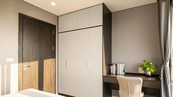A modern bedroom with a large wardrobe, a desk with a chair, a potted plant, and a bedside table.
