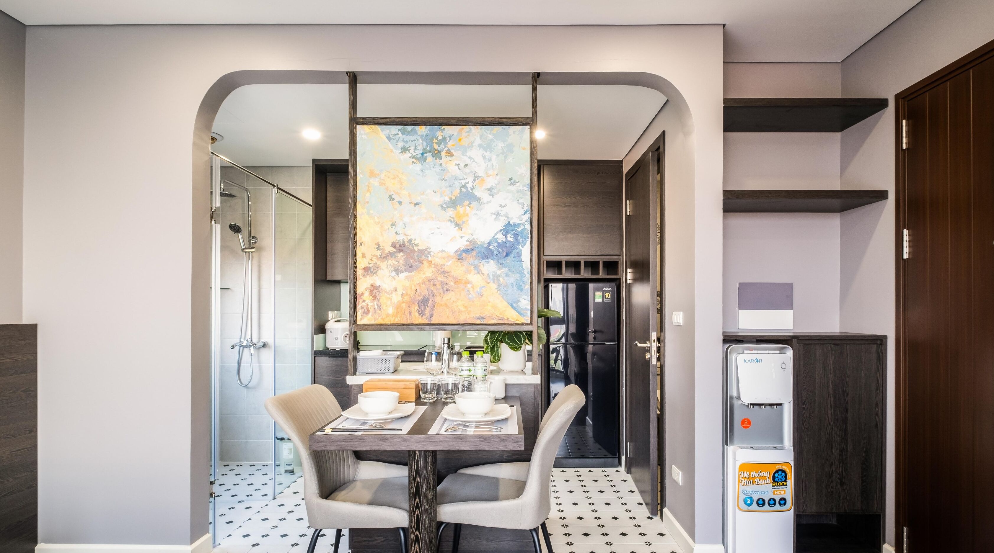A modern hotel room with a dining area, a shower, a refrigerator, and a water dispenser.