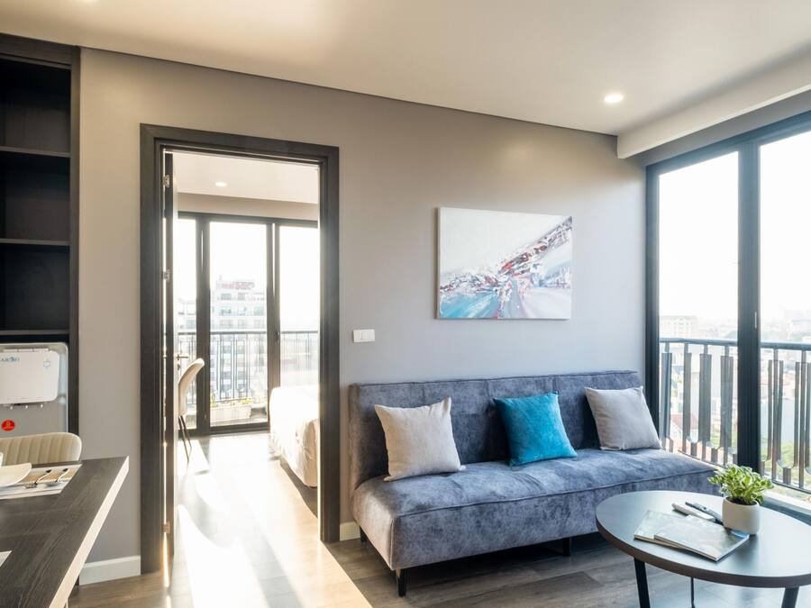 Ein modernes Wohnzimmer mit einem grauen Sofa, einem Esstisch mit weißer Schüssel und Besteck, einem Couchtisch mit Pflanze und einem großen Fenster mit Blick auf die Stadt.
