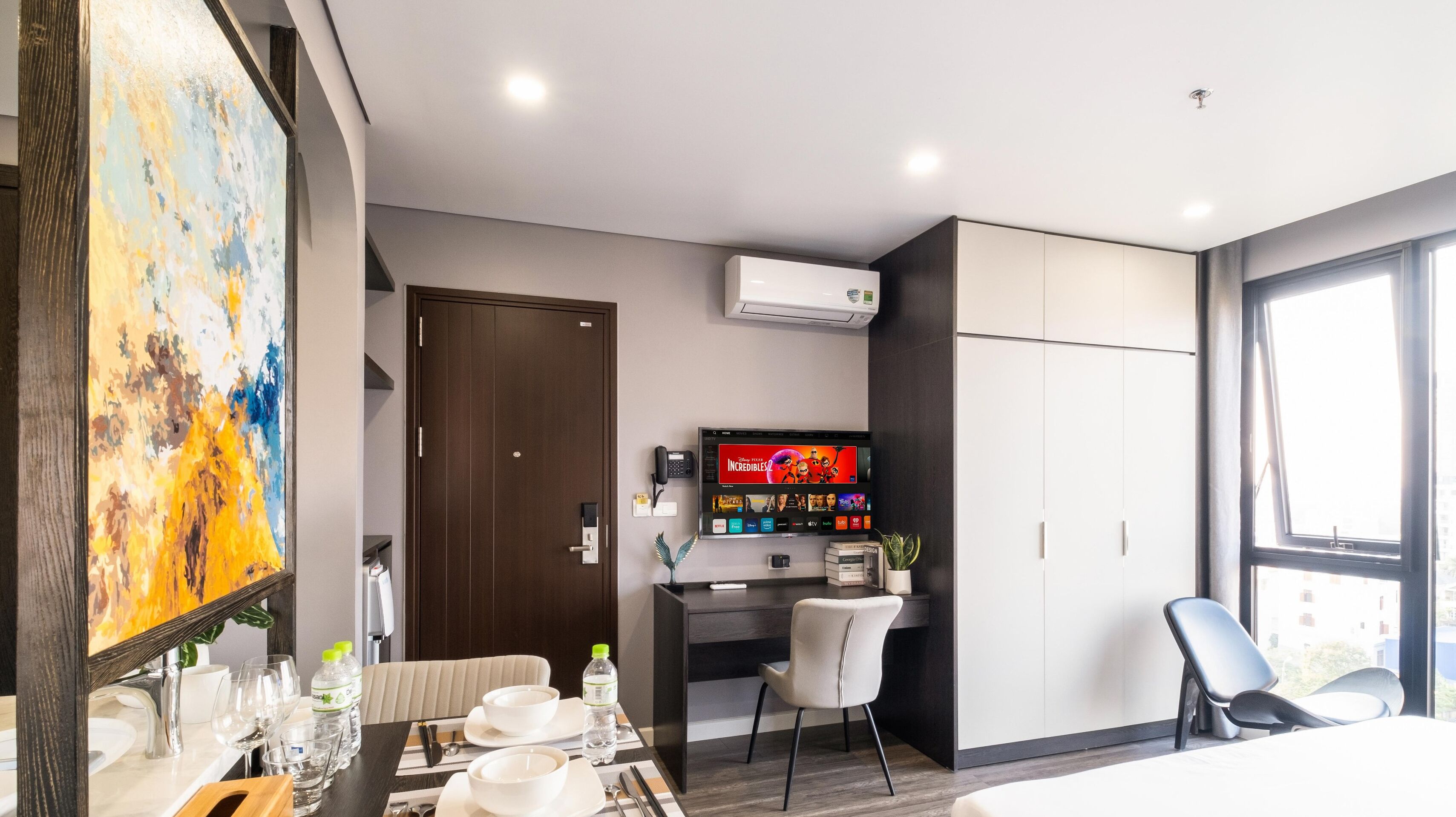 Une chambre d’hôtel moderne dotée d’un coin repas, d’un téléviseur diffusant le film « Les Indestructibles 2 », et d’une grande fenêtre offrant une vue panoramique.