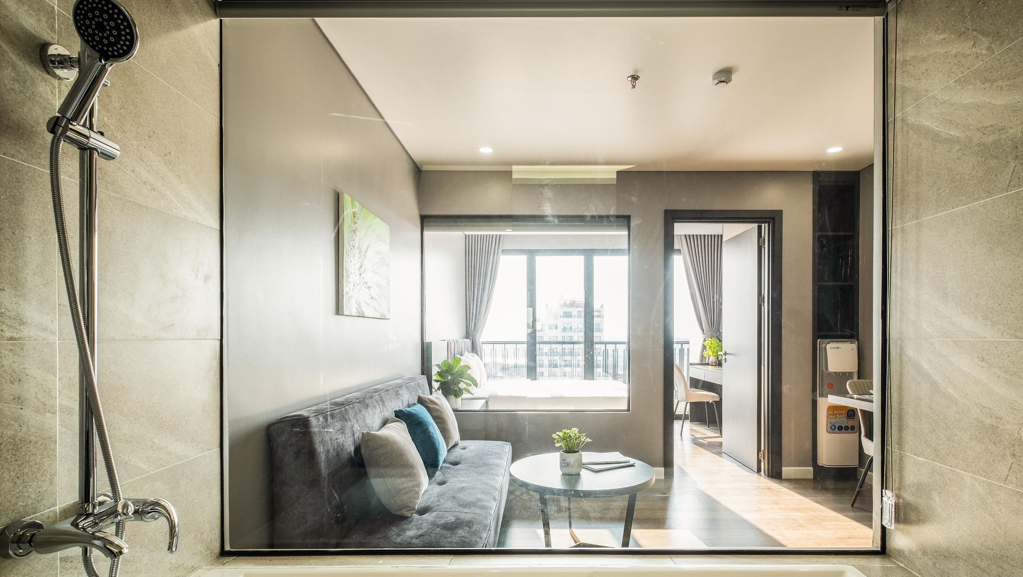 Ein modernes Badezimmer mit Dusche, ein gläserner Wohnbereich mit Sofa und Couchtisch sowie ein Blick auf die Stadt durch große Fenster.