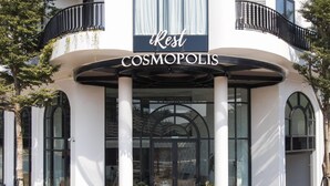 A hotel entrance with a sign reading "iRest COSMOPOLIS" and a covered entrance area with columns and potted plants.