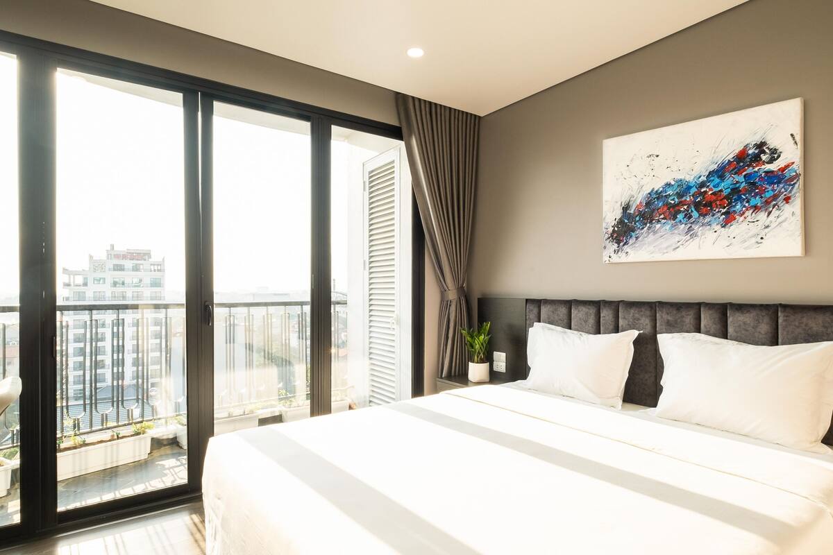 Ett modernt hotellrum med en stor säng, utsikt över staden genom fönster som sträcker sig från golv till tak och en samtida, abstrakt målning på väggen.