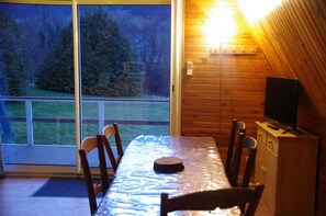 A wooden cabin interior with a dining table, chairs, a television on a wooden cabinet, and a sliding glass door leading to a deck with a view of trees and grass. - QUIET MOUNTAIN CHALET. Hiking, 1/4h from skiing, 200m from the village (Sainte marie de campan)