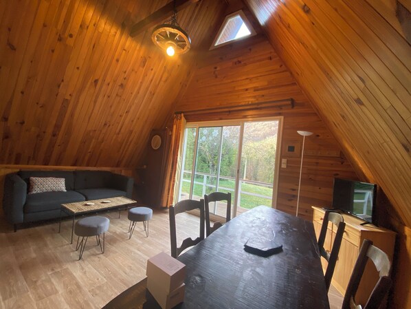 A cozy, wooden-paneled room with a loft-style ceiling, a sofa, a dining table, and a television. - QUIET MOUNTAIN CHALET. Hiking, 1/4h from skiing, 200m from the village (Sainte marie de campan)