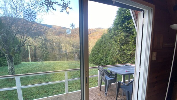 Une terrasse en bois avec une table et des chaises, donnant sur un espace verdoyant agrémenté d’arbres et de collines.
