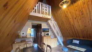 Une pièce mansardée chaleureuse, aménagée avec une table à manger, des chaises, un canapé et un escalier menant à une mezzanine.