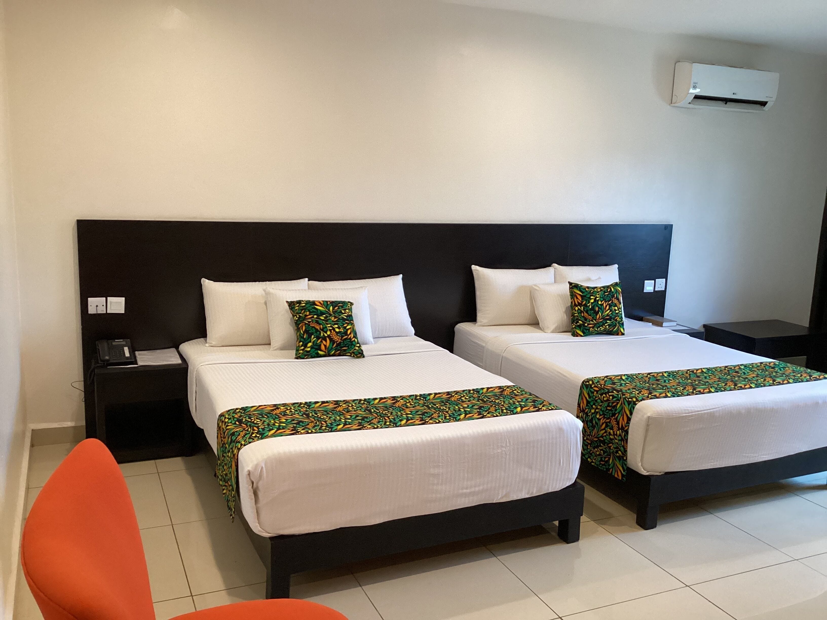 Habitación de hotel con dos camas, una mesita de noche con teléfono, aire acondicionado y una silla.