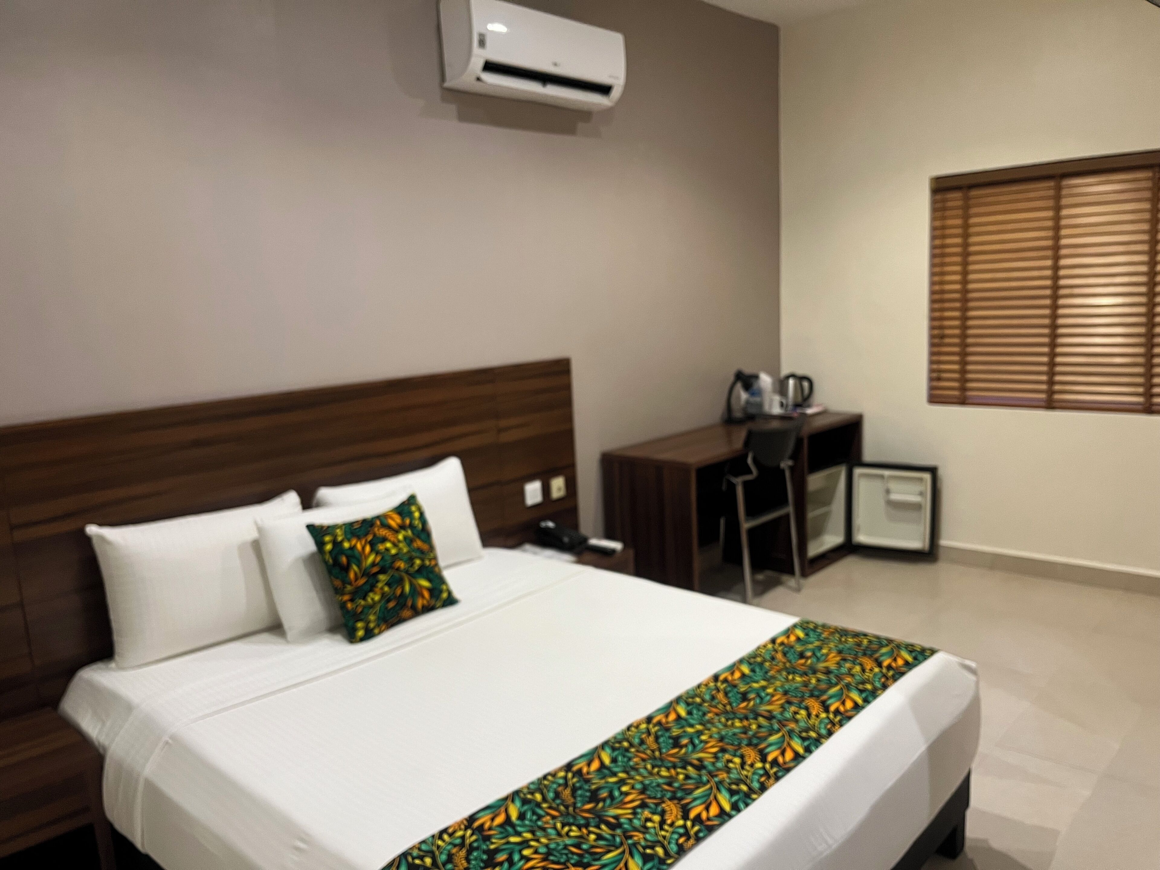 A hotel room with a bed, a desk, a chair, and a window with blinds.