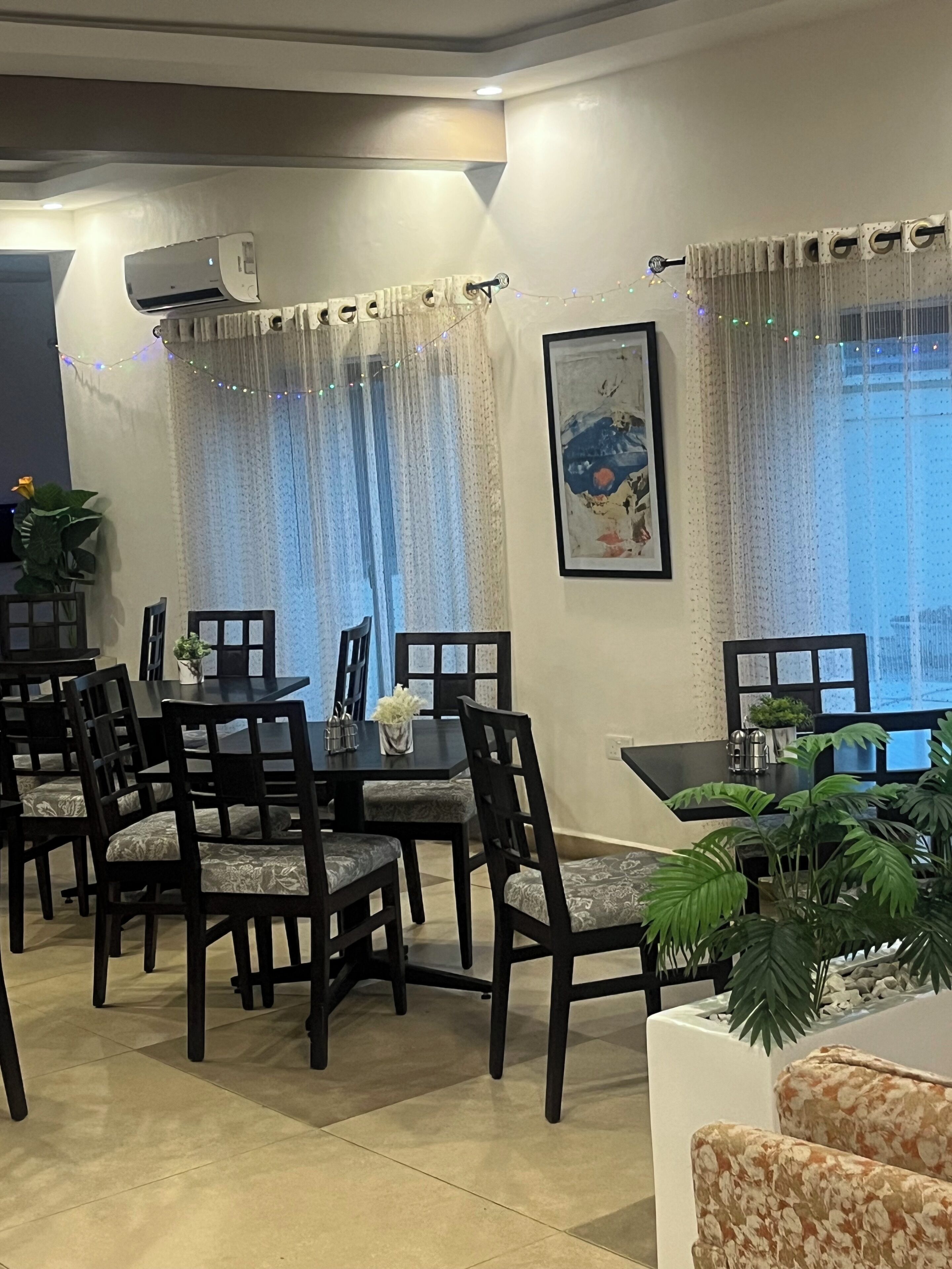 A dining area with a table and chairs, an air conditioning unit, a framed picture on the wall, and a window with curtains.