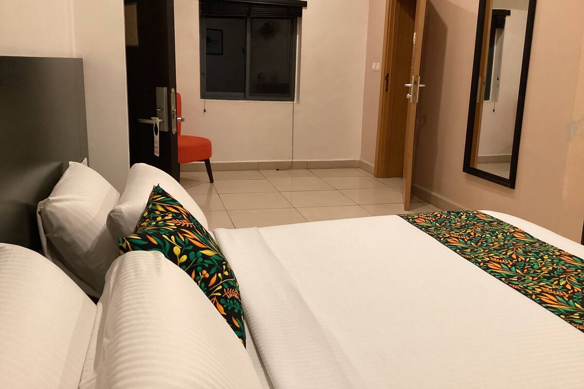 A hotel room with two beds, a chair, a window, and a door.