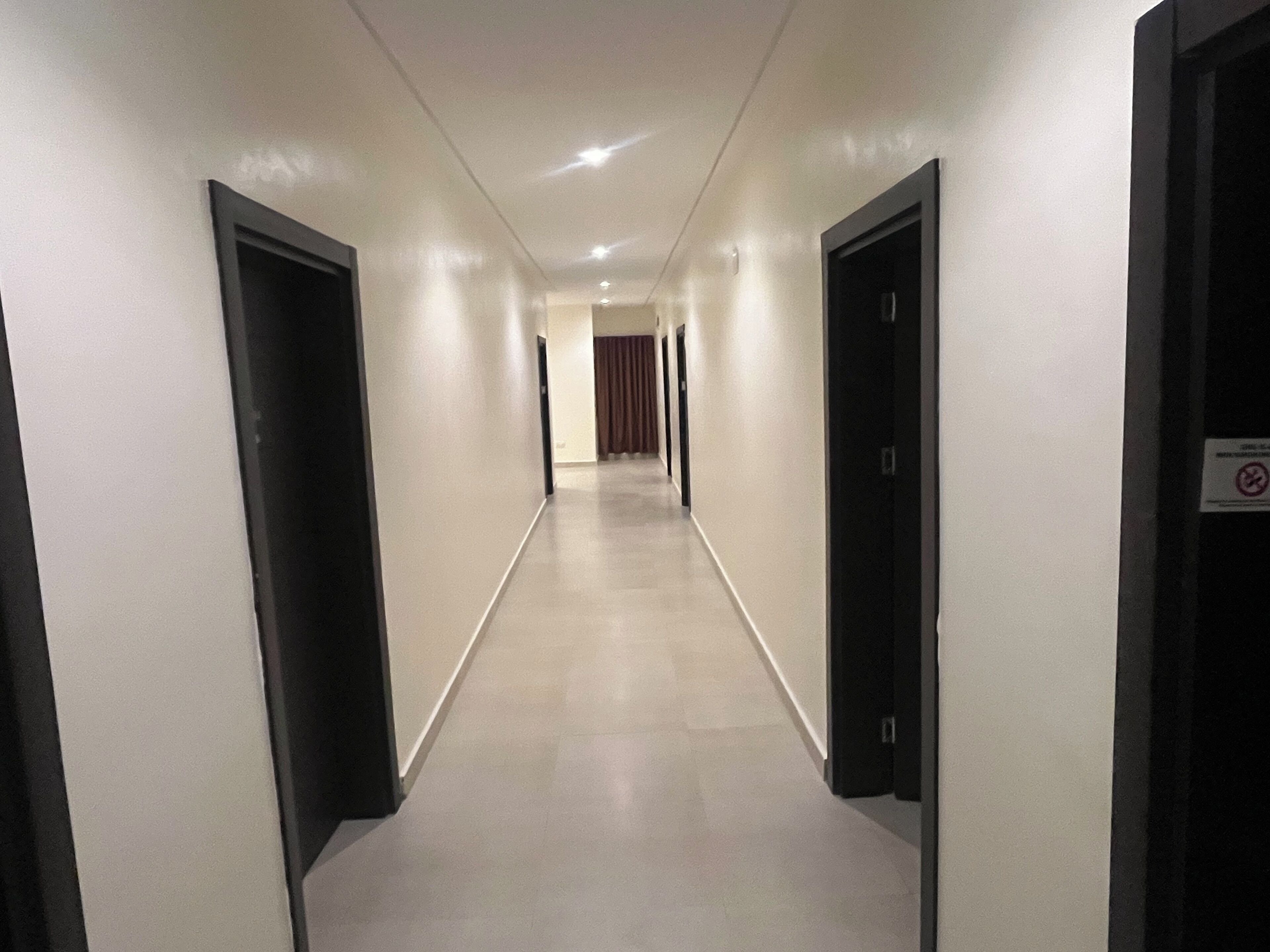 Un pasillo de hotel con puertas a ambos lados, piso de baldosas y un cartel en la puerta derecha.