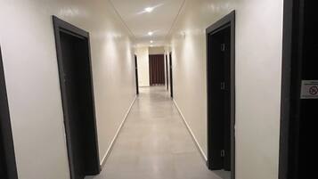Un pasillo de hotel con puertas a ambos lados, piso de baldosas y un cartel en la puerta derecha.
