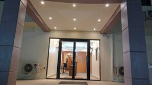 Entrada de un hotel con puerta de vidrio, un mostrador de recepción y dos unidades de aire acondicionado a cada lado.