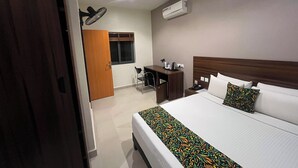 Habitación de hotel con cama, mesita de noche, lámpara, escritorio, silla y unidad de aire acondicionado.