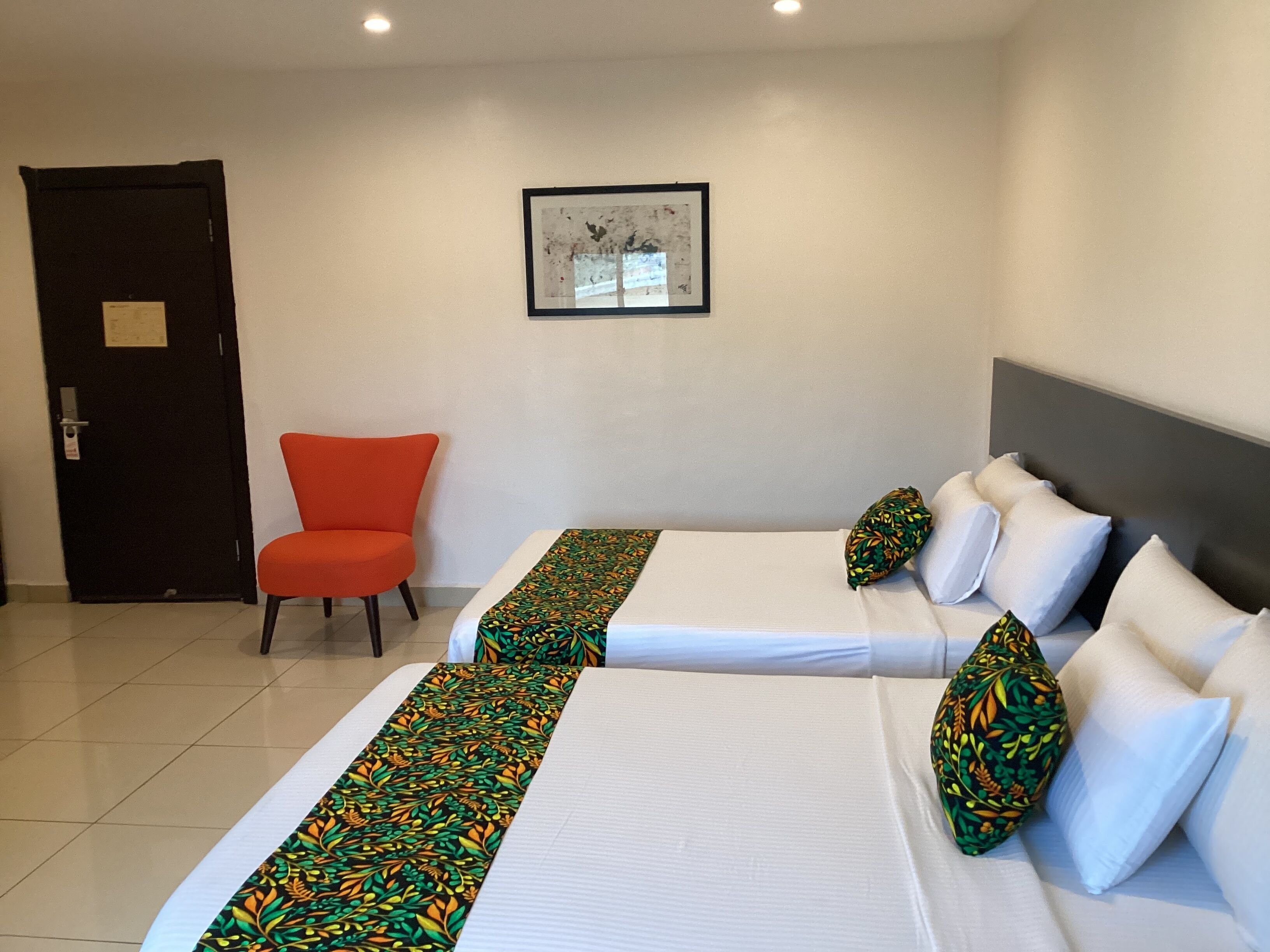 Ein Hotelzimmer mit zwei Betten, einem Sessel, einem gerahmten Bild an der Wand und einer Tür.