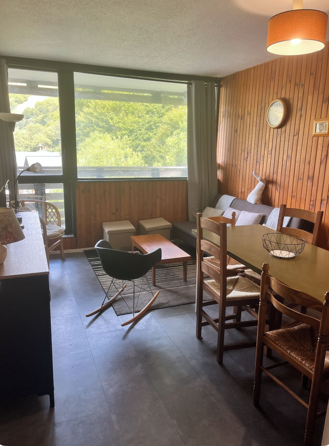 Une pièce comprenant une table à manger, des chaises, un canapé et donnant sur un espace verdoyant.