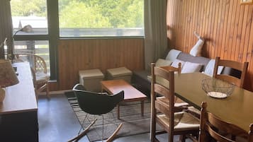 Une pièce comprenant une table à manger, des chaises, un canapé et donnant sur un espace verdoyant.