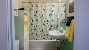 Ein Badezimmer mit Duschvorhang mit Kaktusmuster, einem weißen Waschbecken mit Seifenspender und einer Toilette mit weißem Schrank darüber.