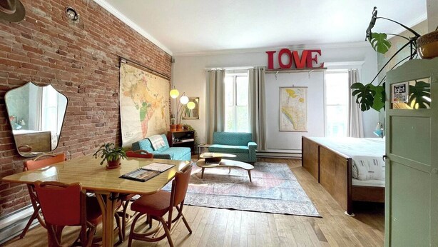 Un salon chaleureux avec un mur en briques, un coin repas avec une table et des chaises en bois, un canapé bleu et une grande carte accrochée au mur.