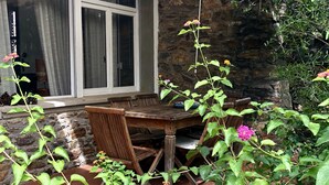 A patio with a wooden table and chairs, a stone wall, and a window with curtains. - A very special villa (Sardegna)