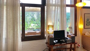 A room with a wooden desk, a computer, a lamp, and a view of greenery outside. - A very special villa (Sardegna)
