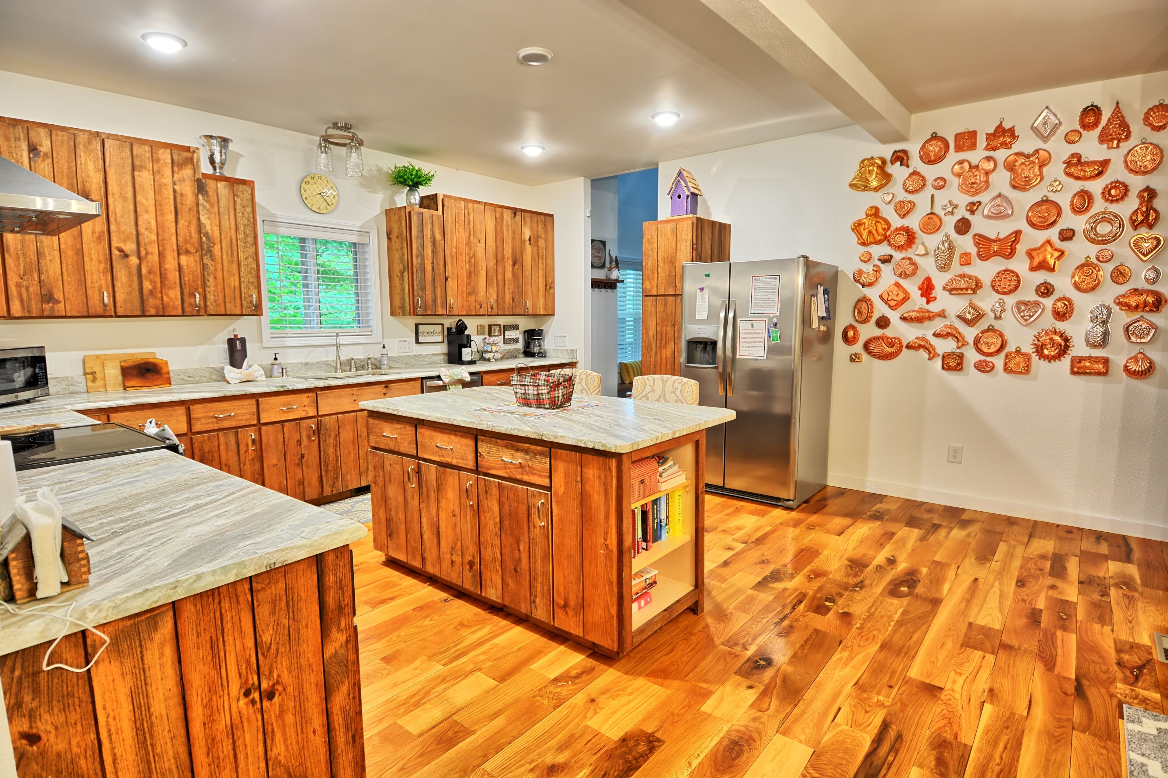 Une cuisine avec des meubles en bois, un îlot central, un réfrigérateur et un mur décoré d’objets d’ornement.