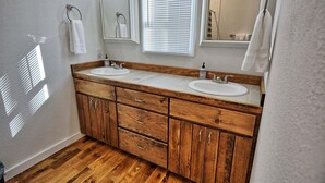 A bathroom with wooden cabinetry, two sinks, a mirror, and a window with blinds. - Escape to Windy Mountain Dreams in Todd, NC—a cozy chalet for 8 with stunning views! (Todd)