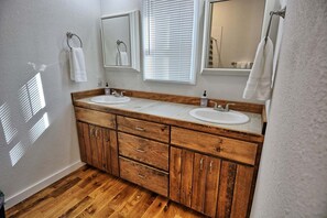 A bathroom with wooden cabinetry, two sinks, a mirror, and a window with blinds.