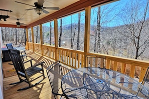 A covered outdoor deck with wooden railings, a table, chairs, and a rocking chair.