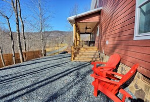 A covered outdoor area with a wooden staircase leading to a building, a gravel driveway, and red Adirondack chairs. - Escape to Windy Mountain Dreams in Todd, NC—a cozy chalet for 8 with stunning views! (Todd)
