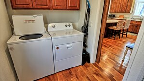 Un espace buanderie compact comprenant un lave-linge et un sèche-linge à chargement frontal, des armoires en bois et un plancher en bois.