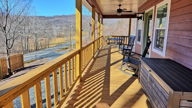 A wooden deck with a railing, a ceiling fan, and a view of a road and trees. - Escape to Windy Mountain Dreams in Todd, NC—a cozy chalet for 8 with stunning views! (Todd)