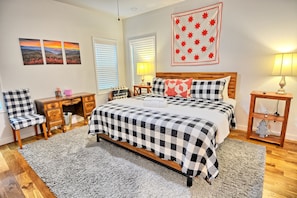 A bedroom with a checkered bedspread, a desk with a chair, a nightstand with a lamp, and a wall with framed artwork. - Escape to Windy Mountain Dreams in Todd, NC—a cozy chalet for 8 with stunning views! (Todd)