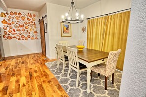 A dining area with a wooden table, white chairs, a chandelier, and a yellow curtain. - Escape to Windy Mountain Dreams in Todd, NC—a cozy chalet for 8 with stunning views! (Todd)