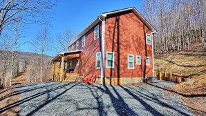A two-story house with a porch, a wooden fence, and a gravel driveway. - Escape to Windy Mountain Dreams in Todd, NC—a cozy chalet for 8 with stunning views! (Todd)
