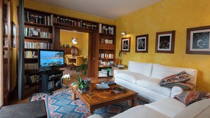 Een woonkamer met een witte bank, een bijzettafeltje, een televisie en boekenplanken vol boeken en trofeeën.