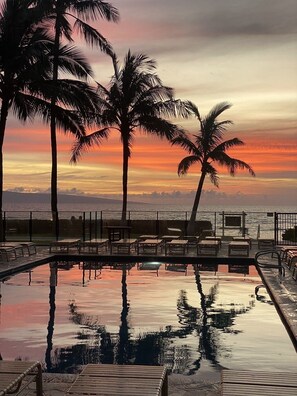 A poolside area with lounge chairs and a view of the ocean at sunset. - Remodeled, Ground floor studio at The Mahana #102 (Lahaina)