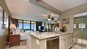 A modern kitchen with a large island, a dining area with a sofa, and a view of the outdoors. - Remodeled, Ground floor studio at The Mahana #102 (Lahaina)