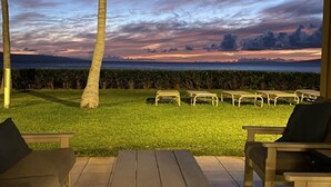 An outdoor seating area with a view of a grassy field and a sunset over the ocean. - Remodeled, Ground floor studio at The Mahana #102 (Lahaina)