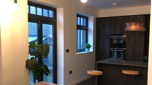 Une cuisine moderne avec une table et un banc en bois, deux tabourets de bar et une fenêtre agrémentée d’une plante.