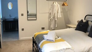 Une chambre à coucher avec un lit, une table de chevet, un miroir et une salle de bain visible à travers une porte ouverte.