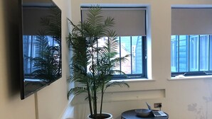 Un salon moderne avec un téléviseur à écran plat, une plante en pot, une table ronde avec un ordinateur portable et une bibliothèque remplie de livres.
