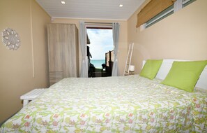 A bedroom with a bed, a window with curtains, a ladder, and a view of the sea. - Beachfront MEERENA, 2 bedroom cottage with Jacuzzi in Calodyne (Calodyne)
