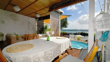 Un'area pranzo all'aperto coperta con piscina, mobili in legno e vista sul mare.
