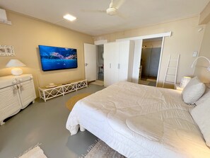 Une chambre à coucher comprenant un lit, une télévision, une armoire et un ventilateur de plafond.
