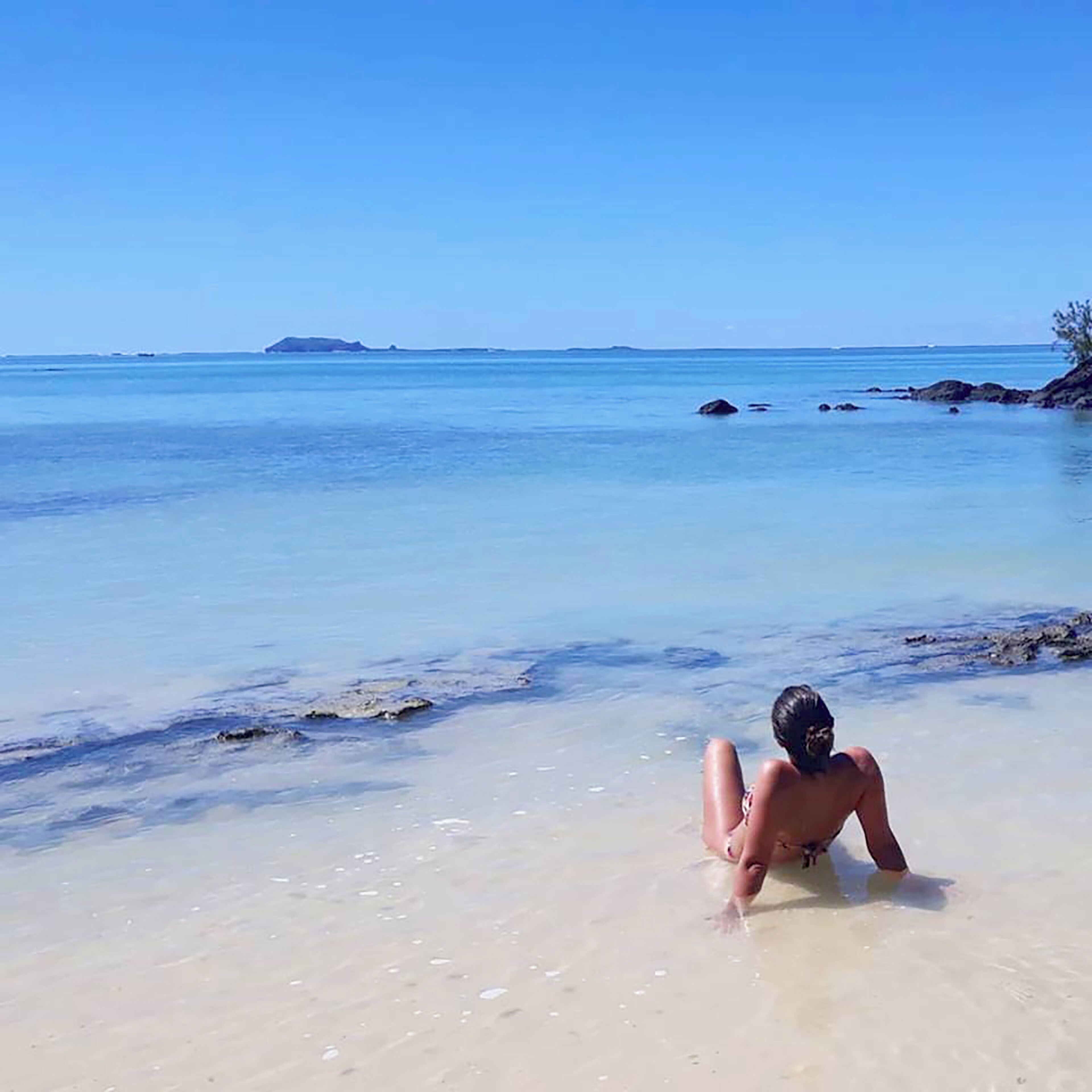 Una spiaggia con acqua cristallina, una persona sdraiata sulla sabbia e isole in lontananza.