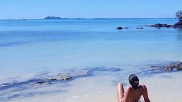Una spiaggia con acqua cristallina, una persona sdraiata sulla sabbia e isole in lontananza.