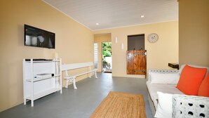A living room with a white sofa, a television mounted on the wall, and a wooden door leading to an outdoor area. - Beachfront MEERENA, 2 bedroom cottage with Jacuzzi in Calodyne (Calodyne)