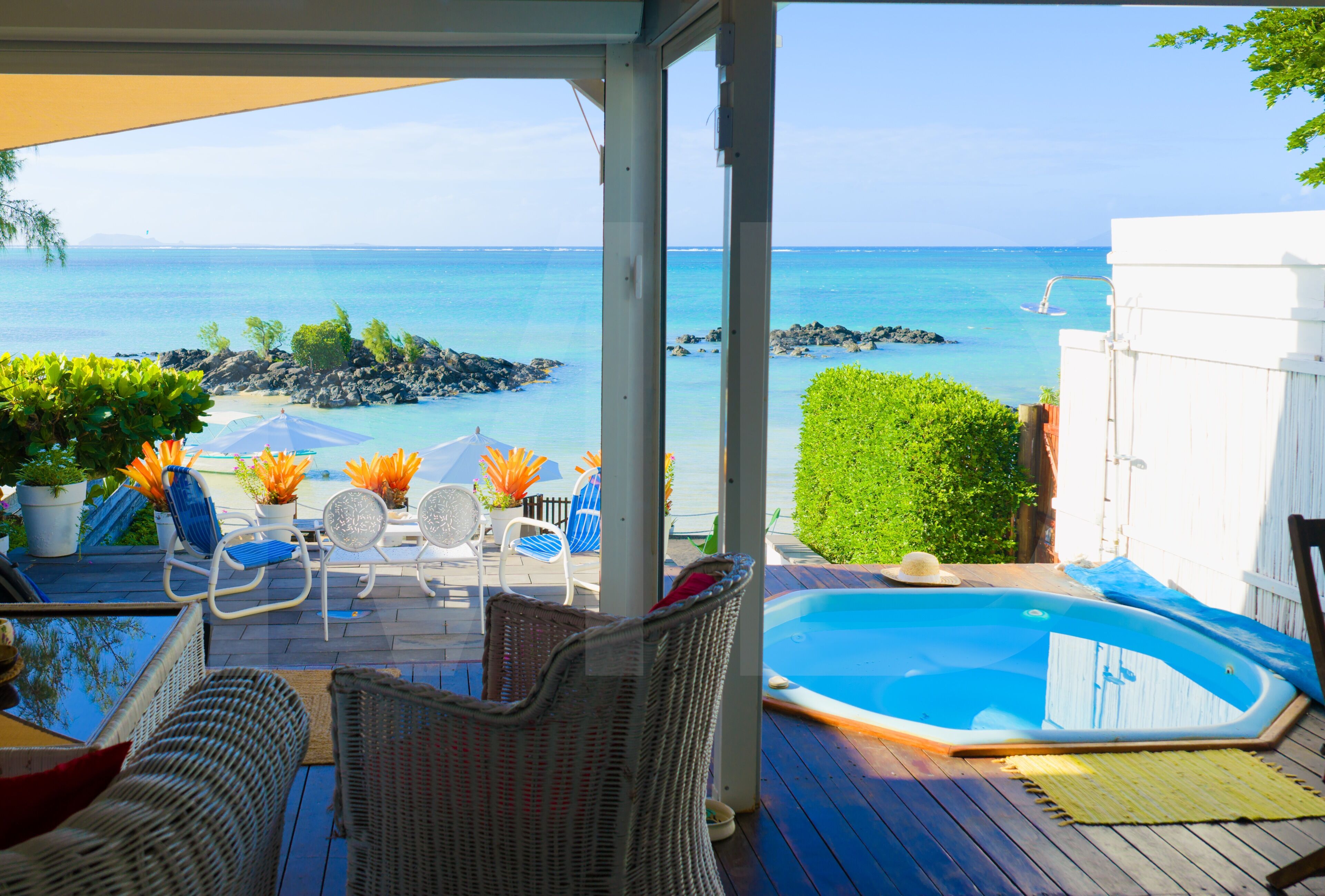A covered outdoor area with a pool, lounge chairs, and a view of the ocean.